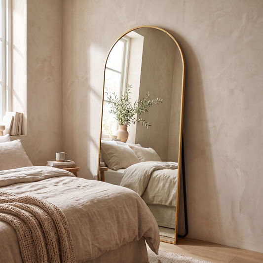 Gold arched full length floor mirror in a warm white bedroom